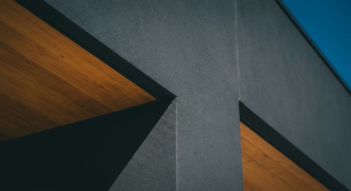 A sharp architectural detail showing a charcoal grey matte wall meeting a natural wood ceiling under a clear sky.