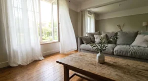 A sunlit living room with an open window and white curtains blowing in the breeze, emphasizing a fresh, airy atmosphere.