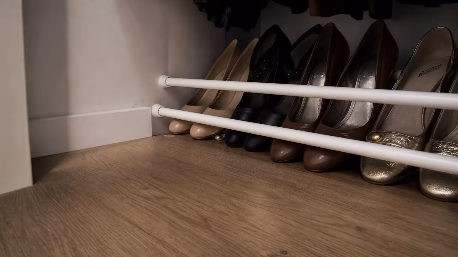 A closet floor with tension rods installed to neatly line up and organize shoes.