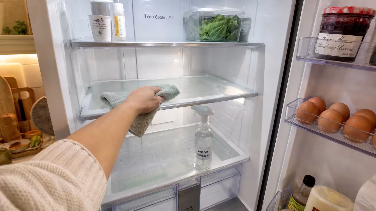 A hand cleaning the glass shelves inside a bright, open refrigerator.