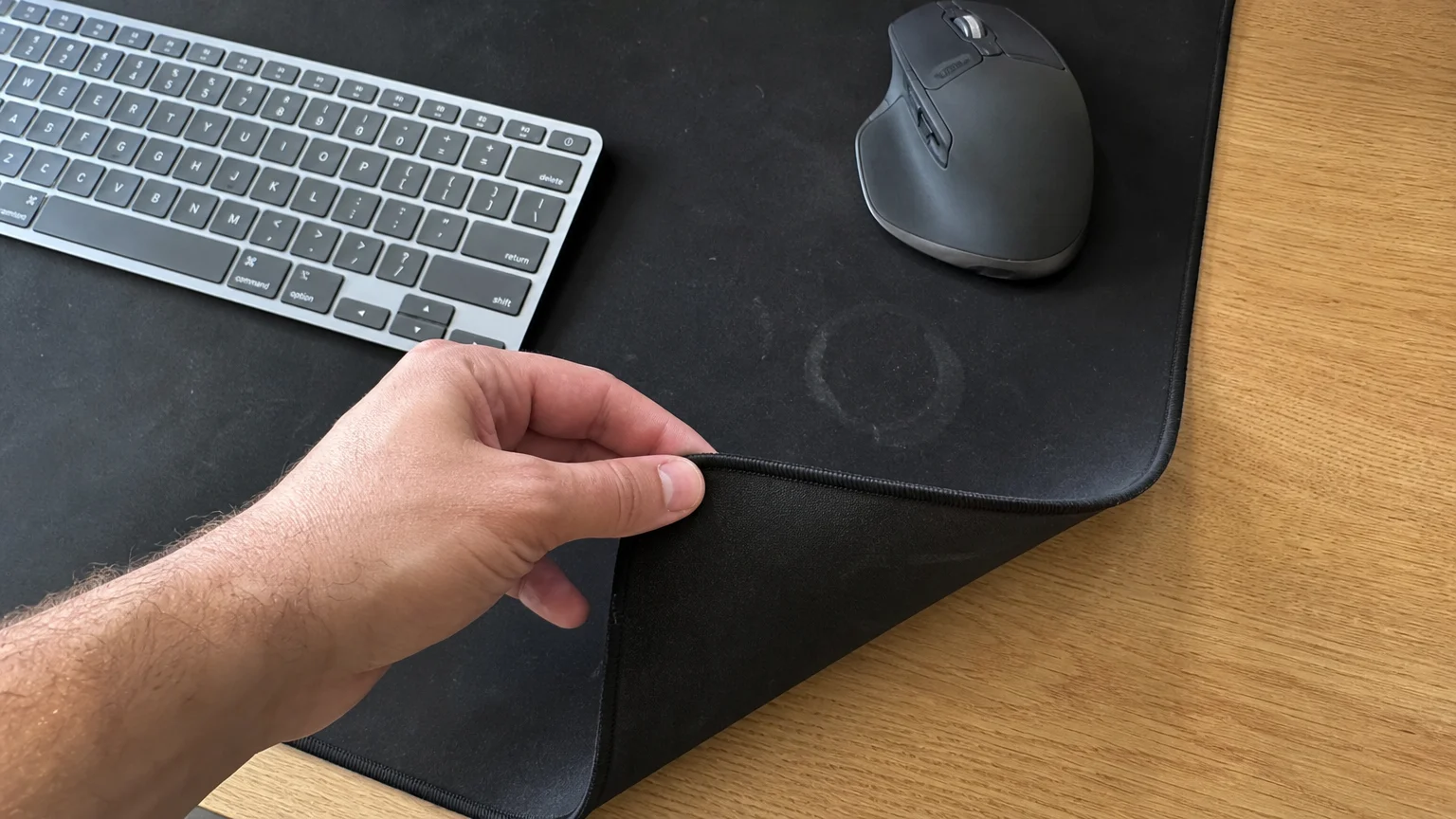 A hand picking up a dirty black cloth desk mat from a wooden desk to take it to the laundry.
