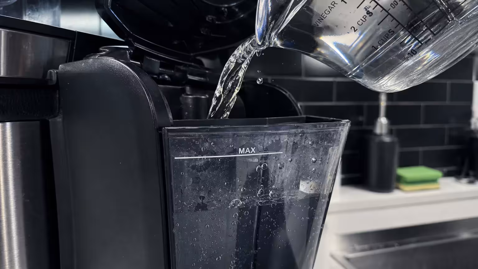 Vinegar being poured into a coffee maker's water tank for descaling.